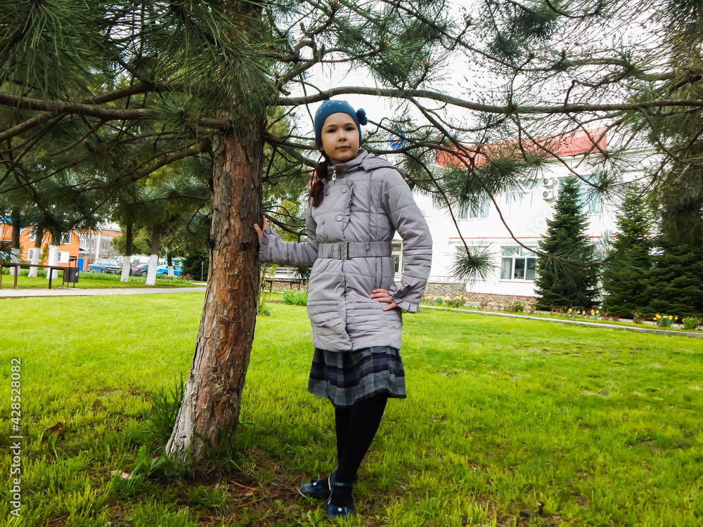 Fototapeta premium a girl in a green clearing next to a coniferous tree