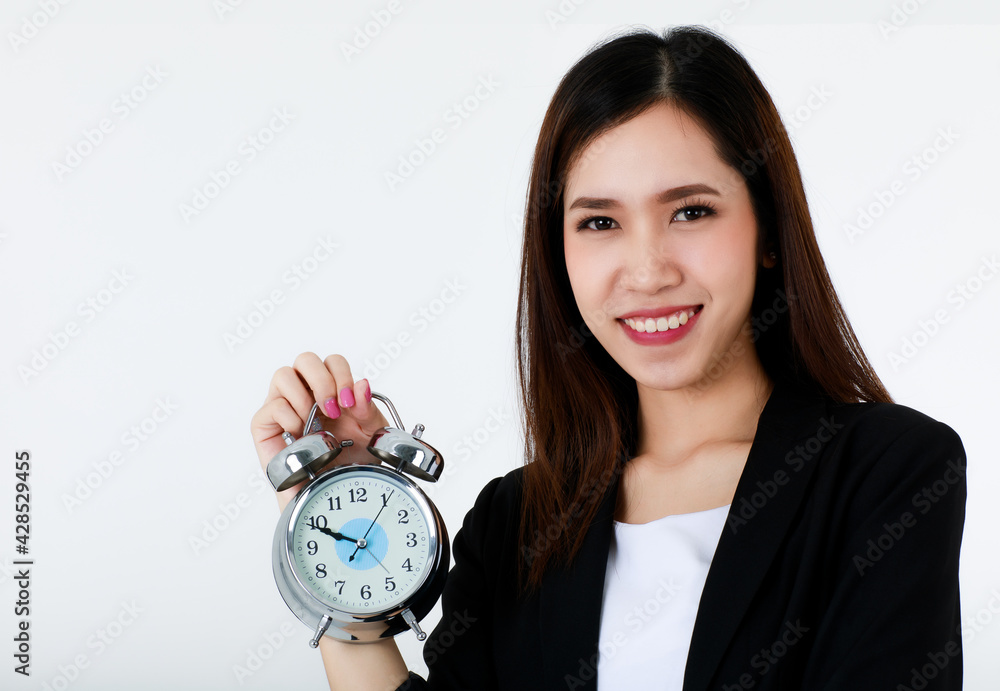 Asian beautiful smiley business woman with long hair wearing formal suit, holding alarm clock and looking to camera with isolated white background. Punctuality, Working hour or busy time concept. Asian beautiful smiley business woman with long hair wearing formal suit, holding alarm clock and looking to camera with isolated white background. Punctuality, Working hour or busy time concept.