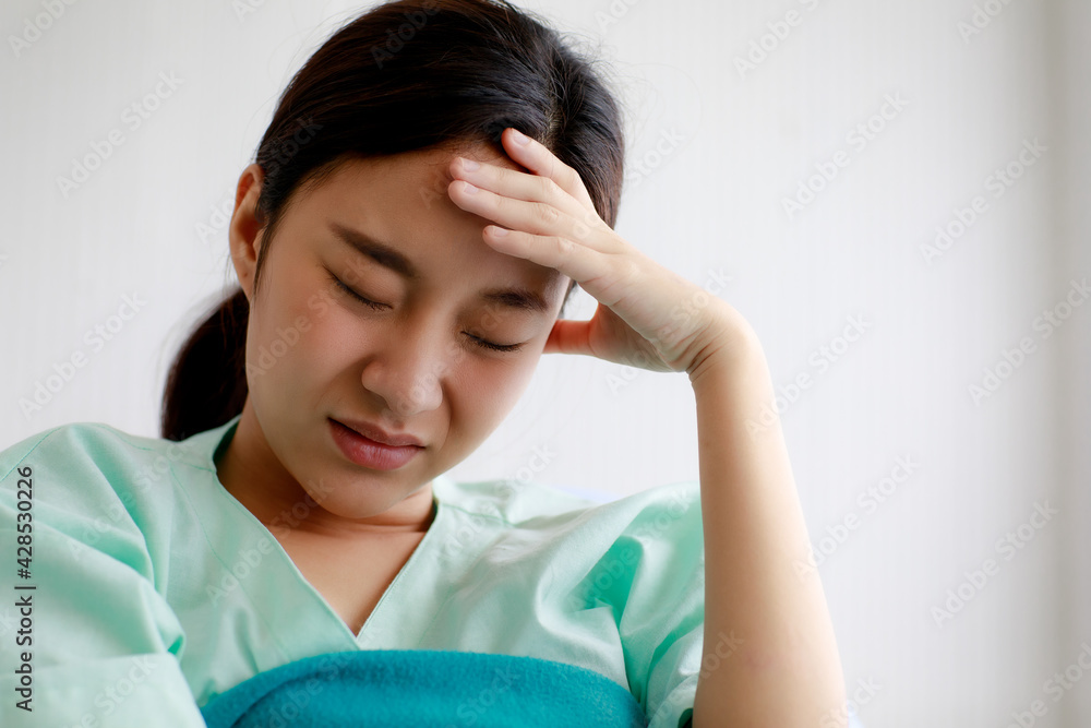 Asian beautiful young female patient getting fever, sick of illness and put her hand on forehead to measure temperature while lying on bed in hospital. Medical Treatment and Health Concept. Asian beautiful young female patient getting fever, sick of illness and put her hand on forehead to measure temperature while lying on bed in hospital. Medical Treatment and Health Concept.