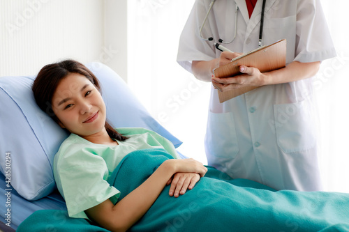 Asian pretty female patient lying on bed in hospital and smiling with happiness while doctor checking her health and report the good result to her. Medical Concept.