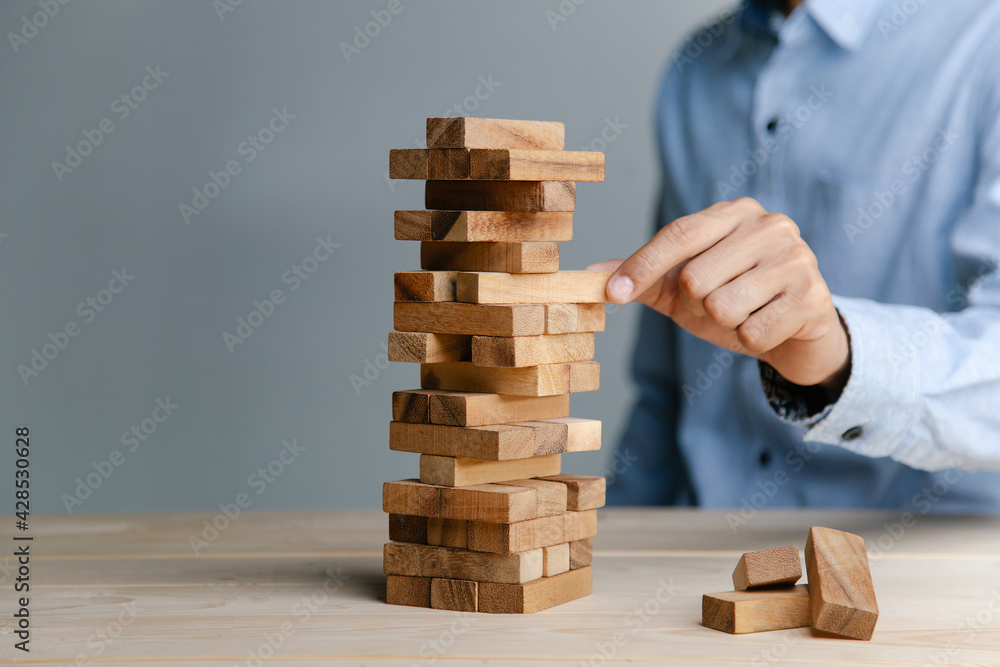 Planning, risk and strategy in business, businessman placing wooden block on a tower. Planning, risk and strategy in business, businessman placing wooden block on a tower.