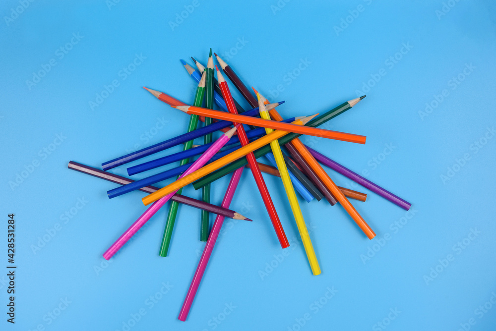 A pile of colored pencils on a blue background. View from above.