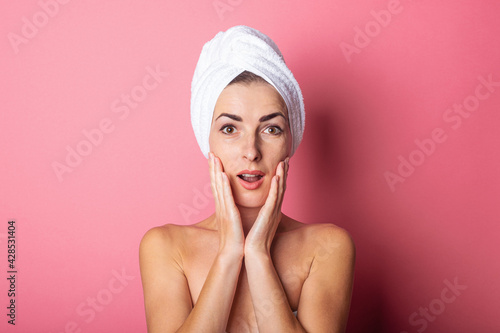 surprised young woman with towel on head, nude shoulders on pink background