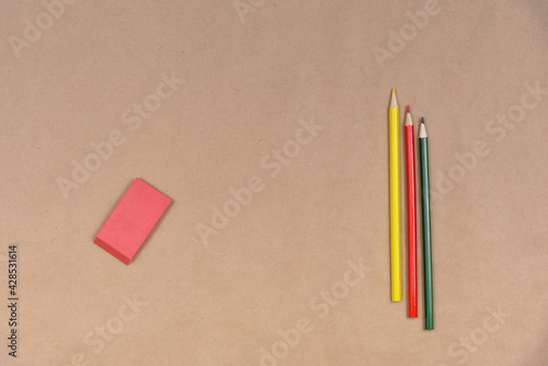 Three colored pencils and one eraser are on craft paper.
