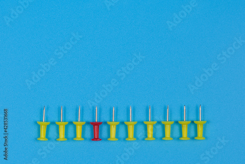 Nine yellow pushpins and one red one lie in a row.