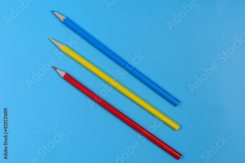 Three colored pencils blue, red and yellow on a light blue background.