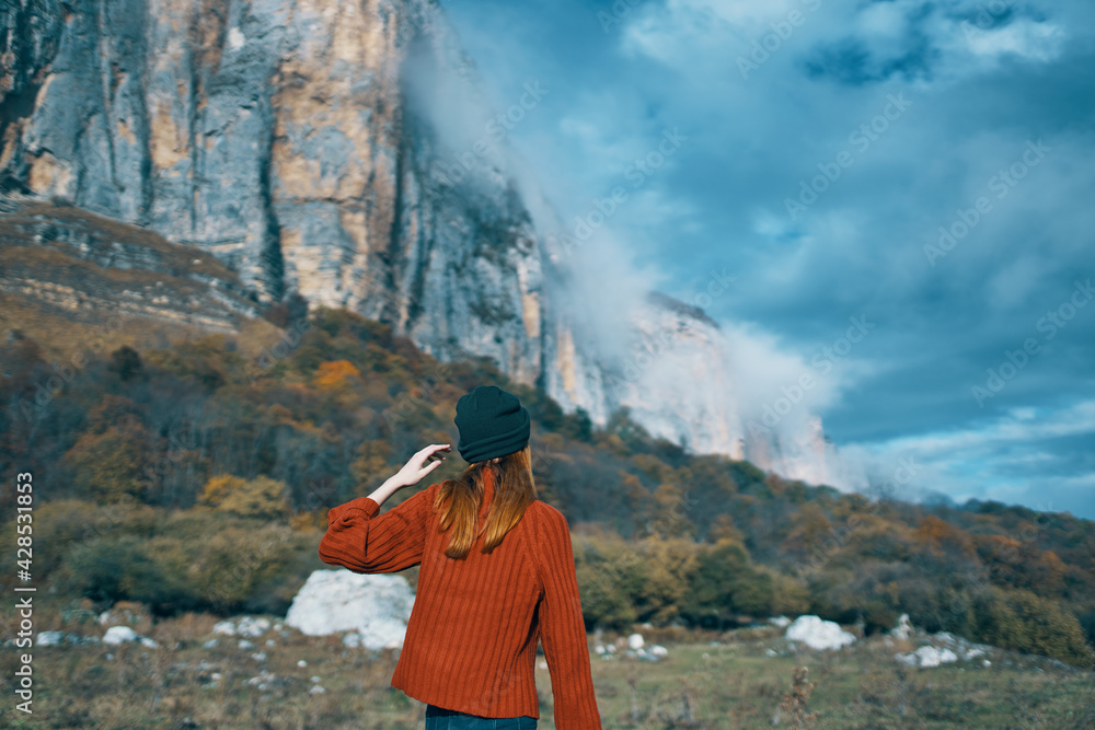 woman in a sweater and jeans with raised up arms travels in the mountains on nature landscape