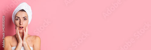 surprised young woman with towel on head touching soft skin on pink background. Banner.