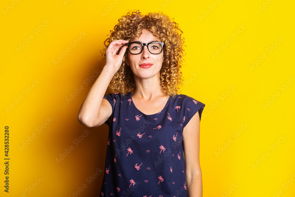 smiling curly young woman in transparent glasses on a yellow background smiling curly young woman in transparent glasses on a yellow background