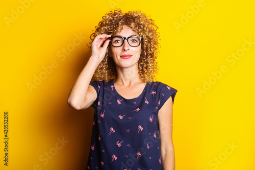 smiling curly young woman in transparent glasses on a yellow background