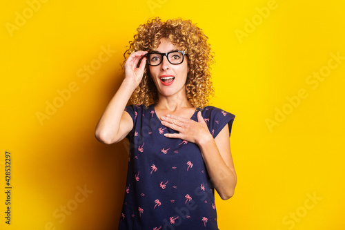 curly young woman in shock, surprised with glasses on a yellow background