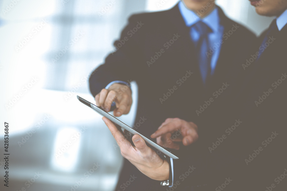 Business people use a tablet computer for discussion of their new project, standing in a modern office. Unknown businessman or male entrepreneur with a colleague at workplace. Teamwork and partnership