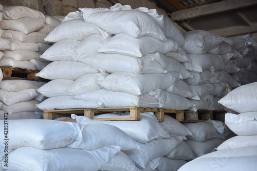 Gray bags of salt are stacked on wooden pallets in straight rows, a factory warehouse.