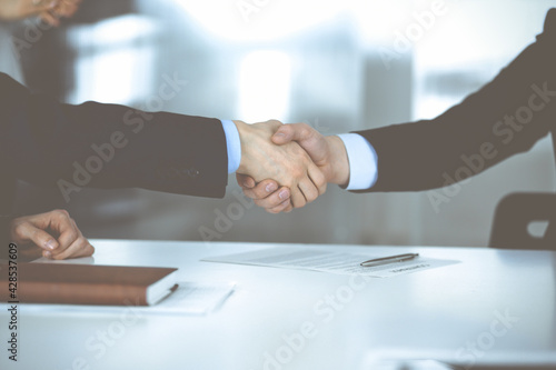 Business people shaking hands at meeting or negotiation, close-up. Group of unknown businessmen, and a woman on the background in a modern office. Teamwork, partnership and handshake concept