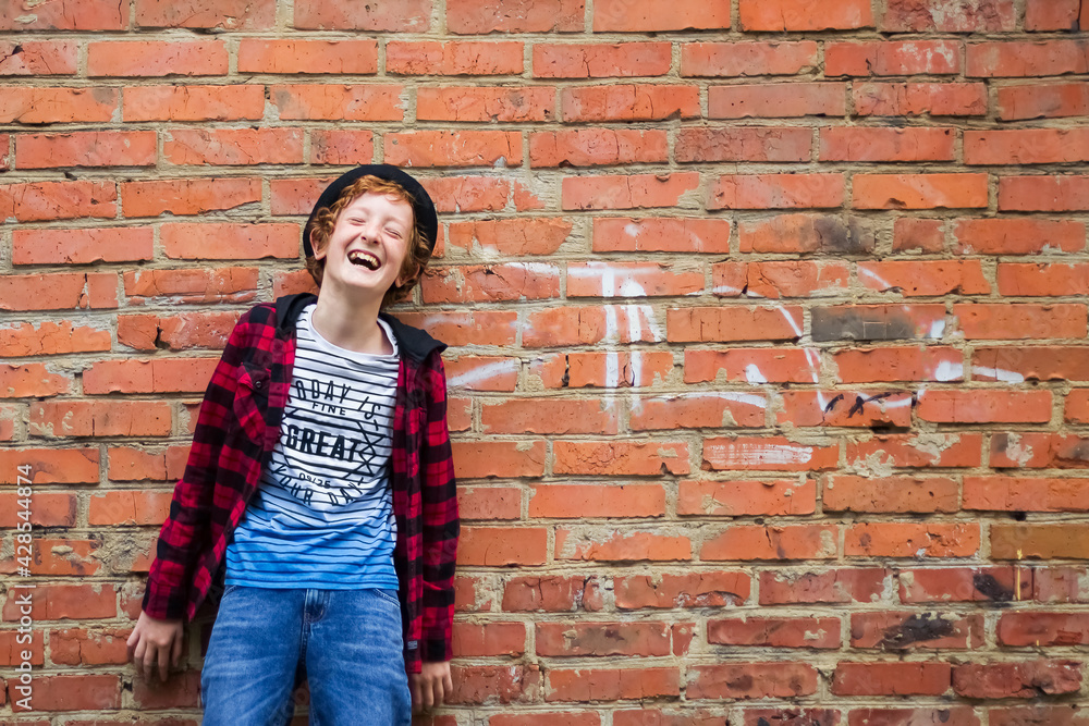 Empty space for the text. A boy 11-13 stands against a wall of red bricks and laughs. Soft focus. Empty space for the text. A boy 11-13 stands against a wall of red bricks and laughs. Soft focus.