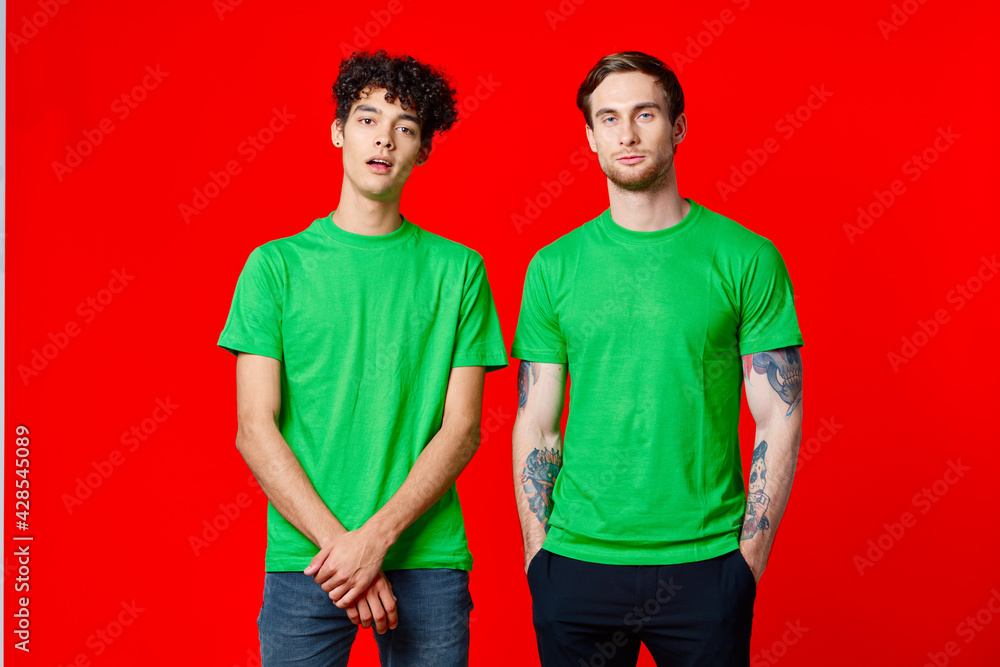 joyful friends in green t-shirts are standing next to red background joyful friends in green t-shirts are standing next to red background