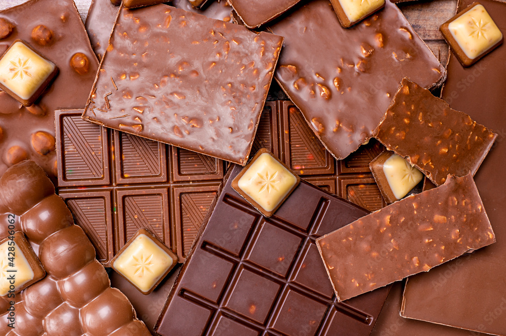 Hazelnut and almond milk and dark chocolate pieces. Top view of pieces of chocolate bar with chocolate chips background. Hazelnut and almond milk and dark chocolate pieces. Top view of pieces of chocolate bar with chocolate chips background.