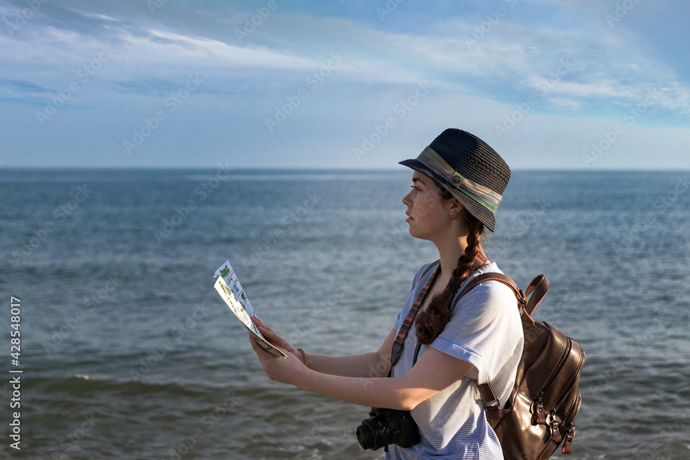 the girl with the camera, backpack and hat looking at the map