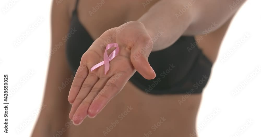 Blurred shot of unrecognizable woman in bra with clenched fist. Woman opens her palm and showing pink ribbon. Symbol of breast cancer awareness. Isolated on white background Blurred shot of unrecognizable woman in bra with clenched fist. Woman opens her palm and showing pink ribbon. Symbol of breast cancer awareness. Isolated on white background