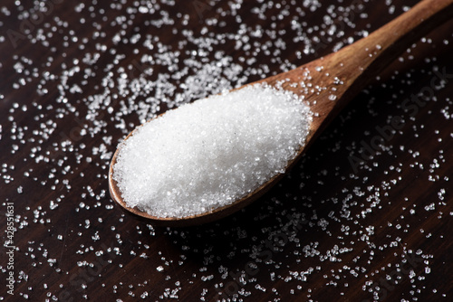 Spoon with white sugar on wood background