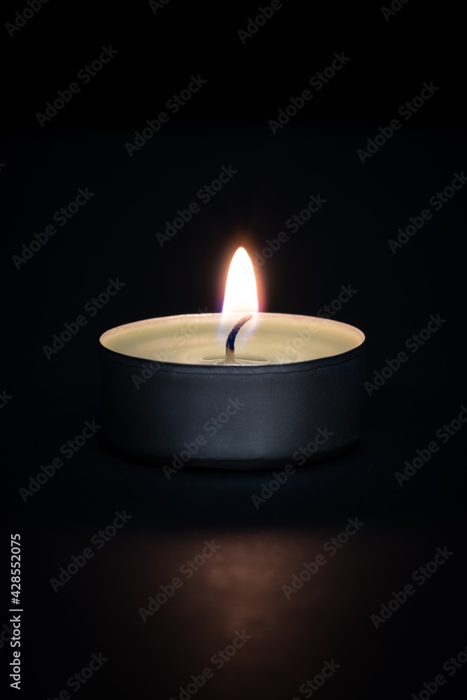 A burning candle on a dark background with a flare in the foreground. A burning candle on a dark background with a flare in the foreground.