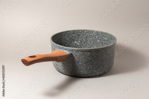 Stone saucepan with wooden handle on solid background.