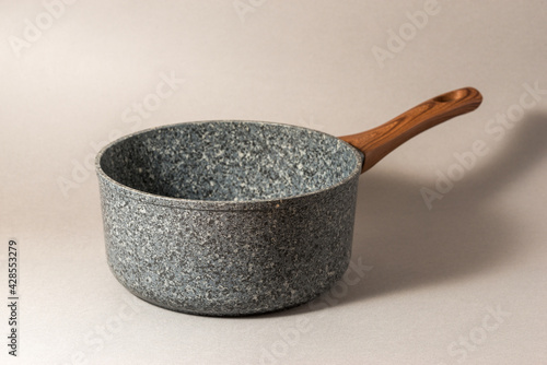Stone saucepan with wooden handle on solid background.