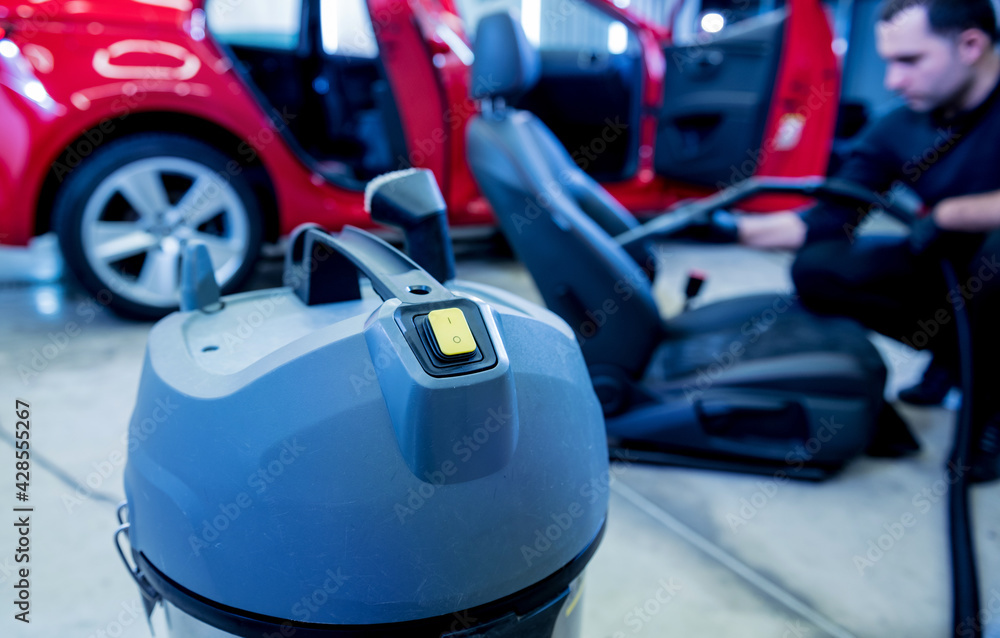 Car service worker cleaning car seat with vacuum cleaner.