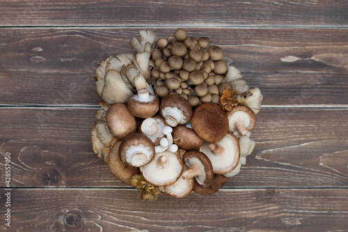 Variety of uncooked wild forest mushrooms in a basket on a wooden old board.