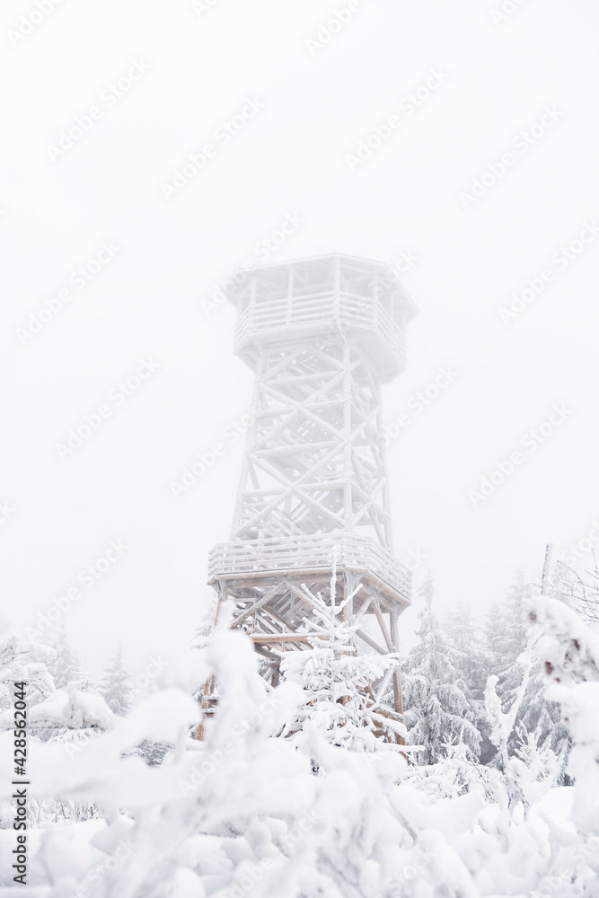 A snow-covered wooden lookout tower on top of the Czernica Mountain. Winter landscape in the Sudetes on a hiking trail. A snow-covered wooden lookout tower on top of the Czernica Mountain. Winter landscape in the Sudetes on a hiking trail.