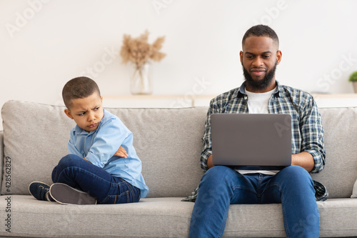 Quadro em tela Reluctant Black Dad Ignoring Offended Son Using Laptop Indoors