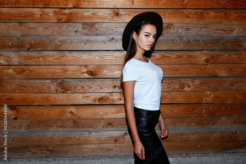 Profile portrait of a fashion girl in hat, her hair straight dressed in leather pants and t shirt near the wooden wall. Profile portrait of a fashion girl in hat, her hair straight dressed in leather pants and t shirt near the wooden wall.
