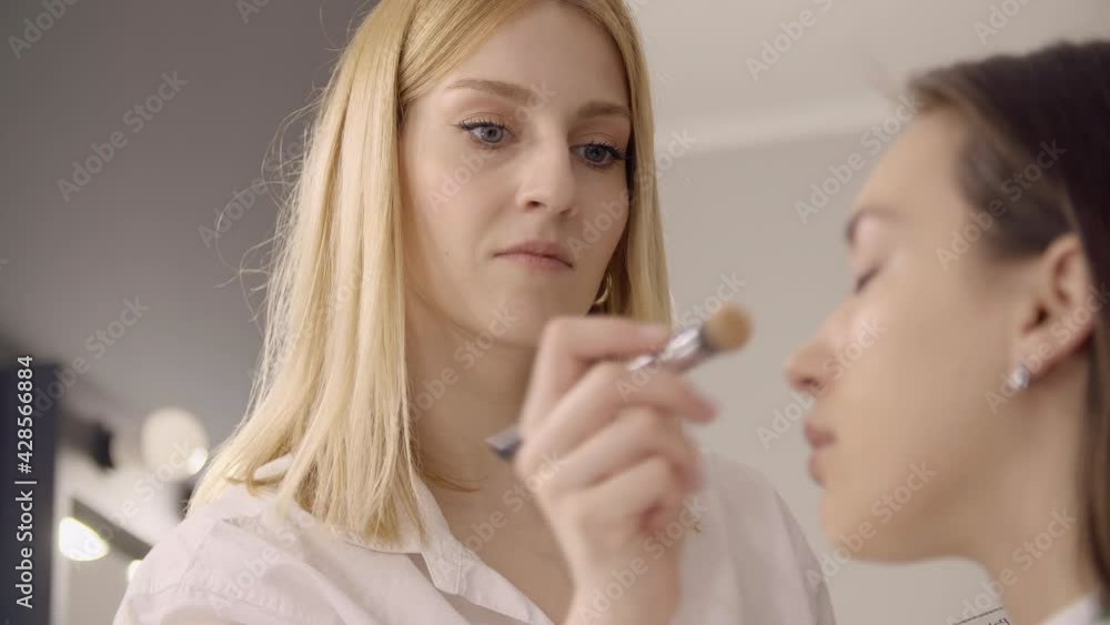 Close-up of a MUA using pink sponge for putting on a cosmetic product. Blonde caucasian woman works in a studio, while preparing a model for fashion show. High quality 4k footage Close-up of a MUA using pink sponge for putting on a cosmetic product. Blonde caucasian woman works in a studio, while preparing a model for fashion show. High quality 4k footage
