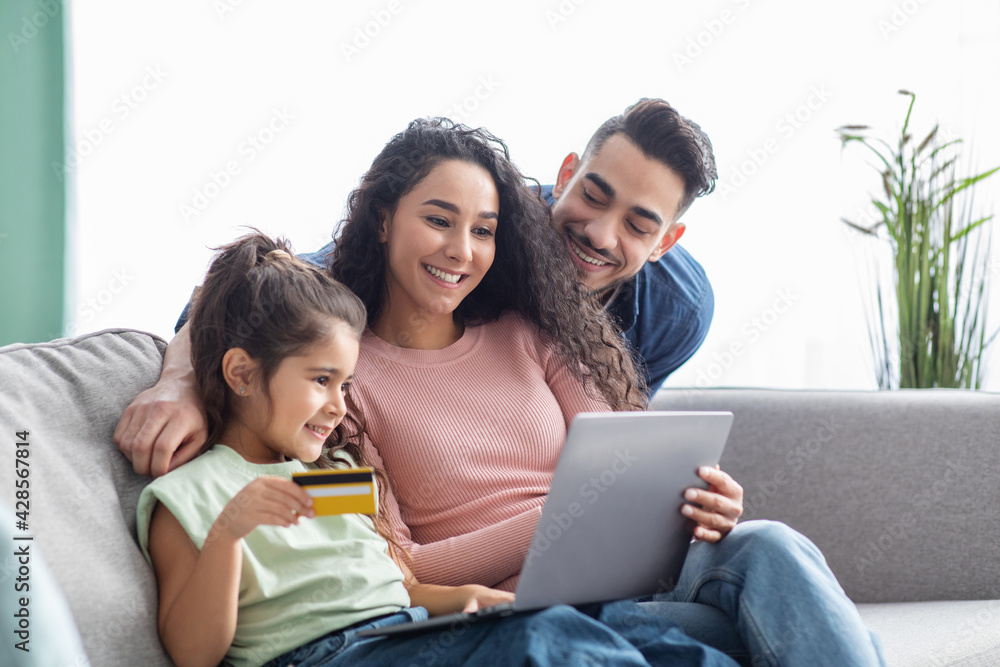 Booking Vacation Online. Happy family using laptop and credit card at home