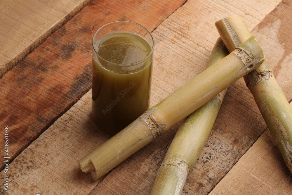 Sugarcane juice in glass with piece of sugarcane on wooden table 