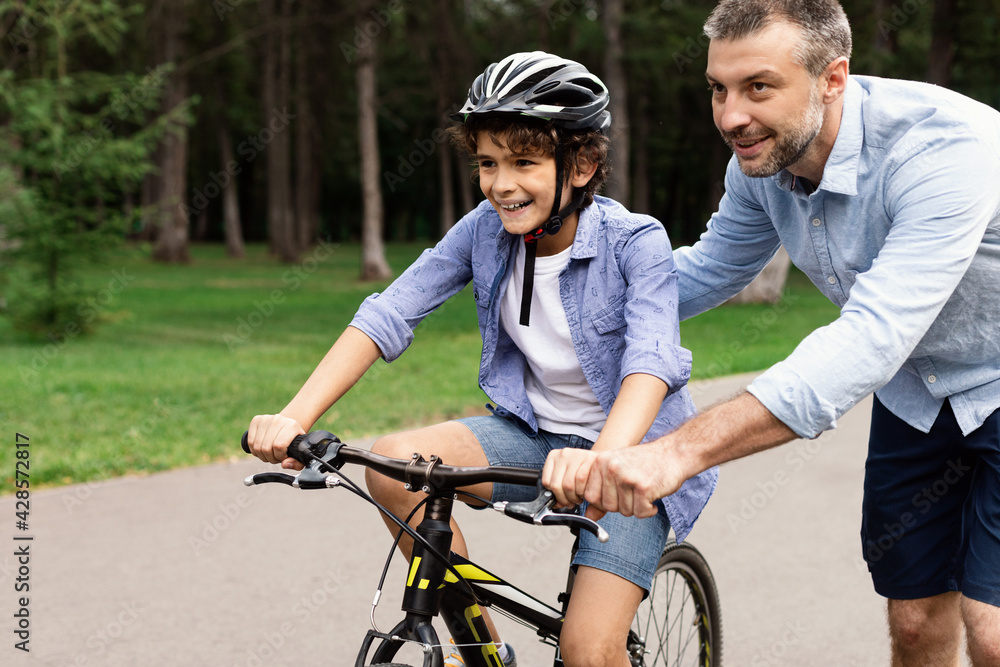 Boy learning how to ride bicycle with his happy dad