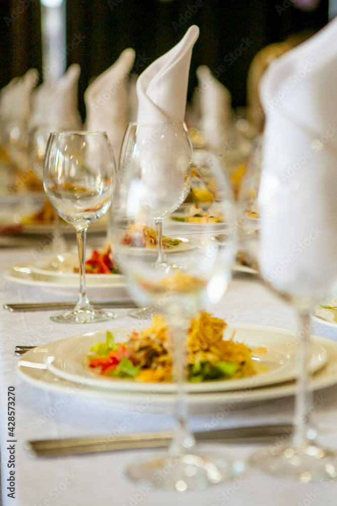 Close-up of a banquet set table: wine / champagne glasses, napkins and salad. For a solemn holiday