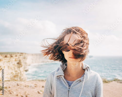 Portrait of a beautiful smiling woman and sea shore in the background. Her hair blows in the wind.