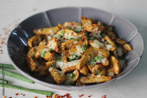 Cheesy potato wedges made by baking air fried potato wedges after sprinkling it with shredded mozzarella, chilli flakes and chopped green onions.