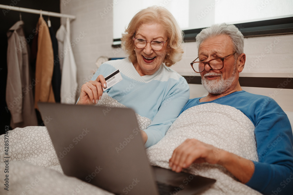Senior couple lying in bed and buying over the Internet by credit card.