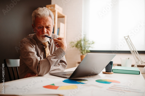 Mature businessman thinking about write news article while working an office.