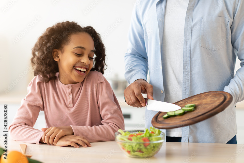 Cheerful afro father and daughter cooking salad together Cheerful afro father and daughter cooking salad together