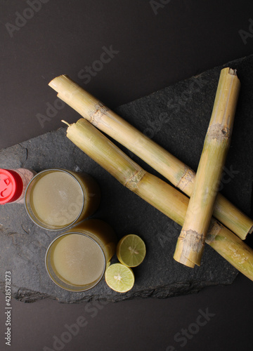 Sugarcane juice in glass with piece of sugarcane, lemon and black salt  photo