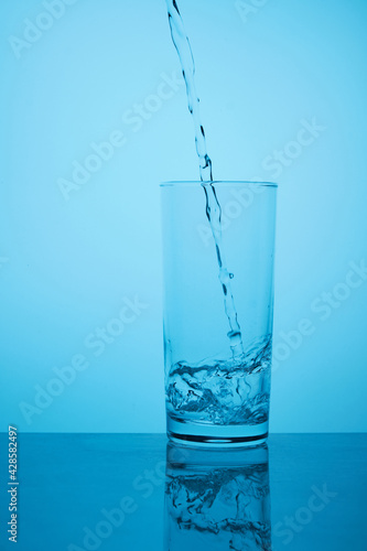 Glass of pure still water. Thirst quenching. Pure still water pours from bottle to glass against blue background with back lighting