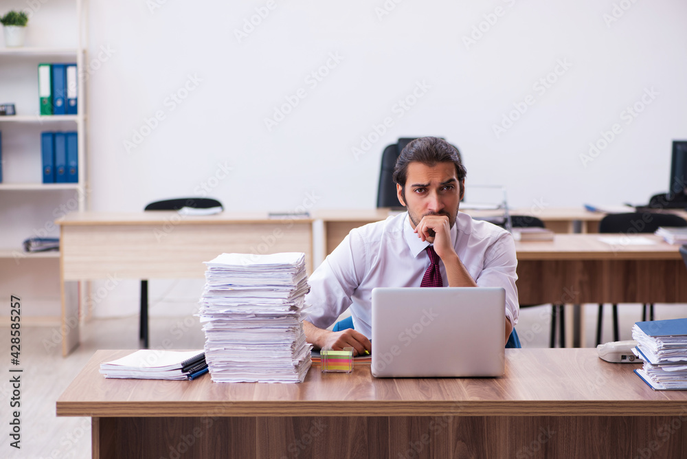 Young male employee unhappy with excessive work in the office Young male employee unhappy with excessive work in the office