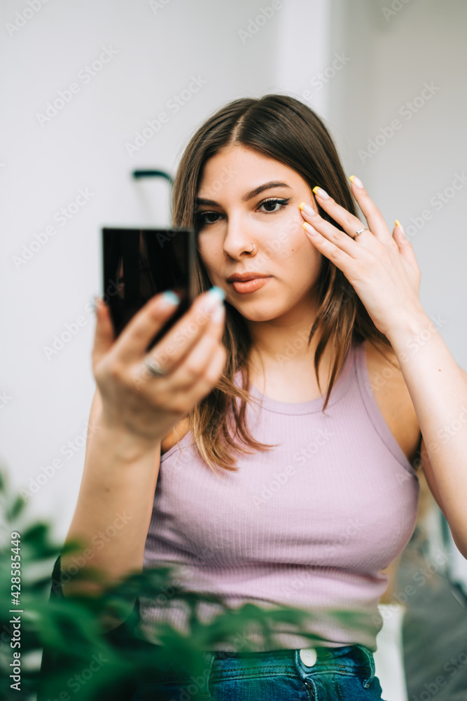 Attractive caucasian young woman holding cosmetic mirror in hand and looking on herself . Attractive caucasian young woman holding cosmetic mirror in hand and looking on herself .
