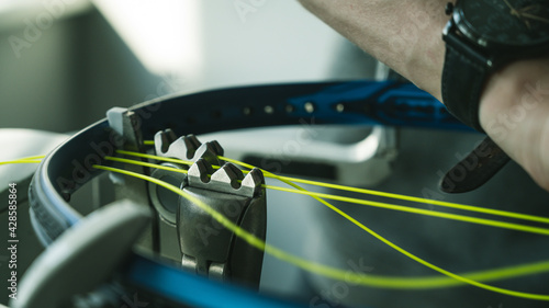 Close-up of tennis racket on electronic stringing machine. Process of replacement synthetic gut string before game. Hands of stringer. photo