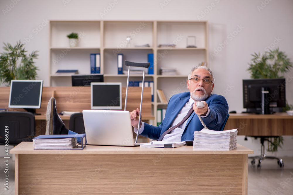 Old businessman employee after accident working in the office Old businessman employee after accident working in the office