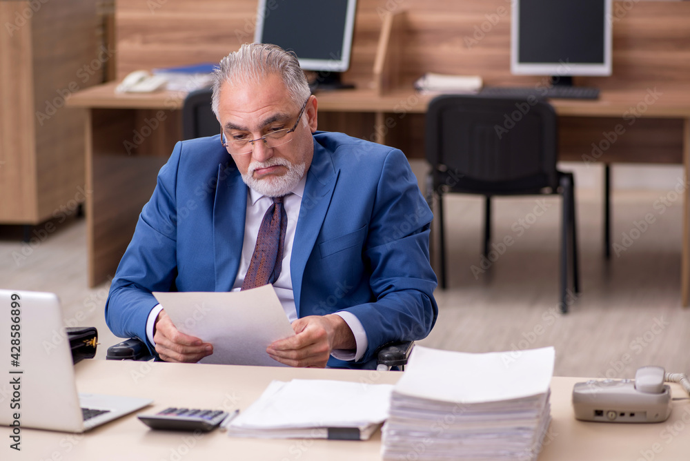Old businessman employee in wheel-chair working in the office Old businessman employee in wheel-chair working in the office