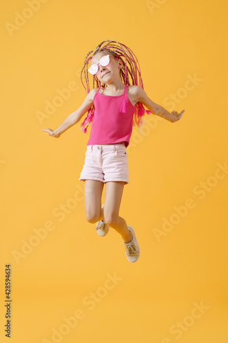 Stylish girl with pink dreadlocks and posing on a yellow backgro